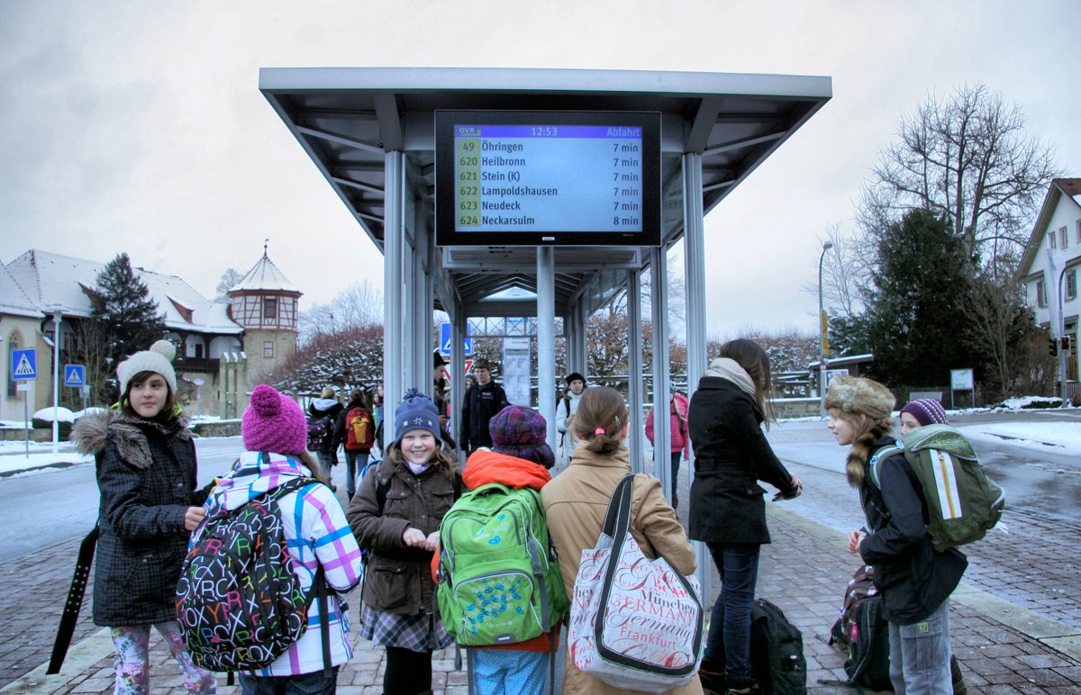 Kinder an Bushaltestelle mit Abfahrtsmonitor