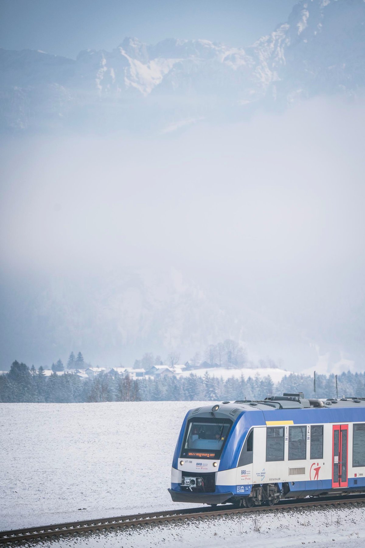 Ein LINT-Zug der BRB fährt am Hopfensee mit Bergen im Hintergrund.